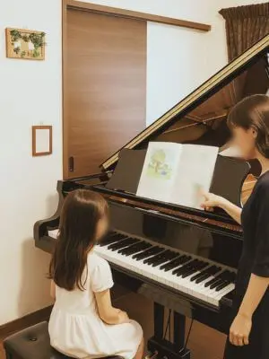 N piano music schoolのベーシックコースで先生の指導を真剣に聞いている女の子。グランドピアノとやさしい雰囲気の教室の様子。