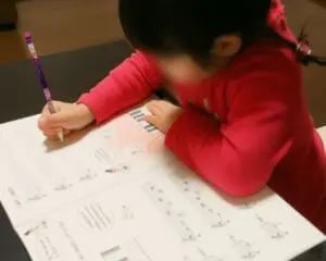 ピアノのワークブックに夢中で取り組む幼い女の子。集中する姿勢が印象的