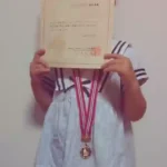 小山市のピアノ教室 N piano music school に通う小学生の生徒が、ピティナ・ピアノコンペティション本選入選証書とメダルを持っている様子。