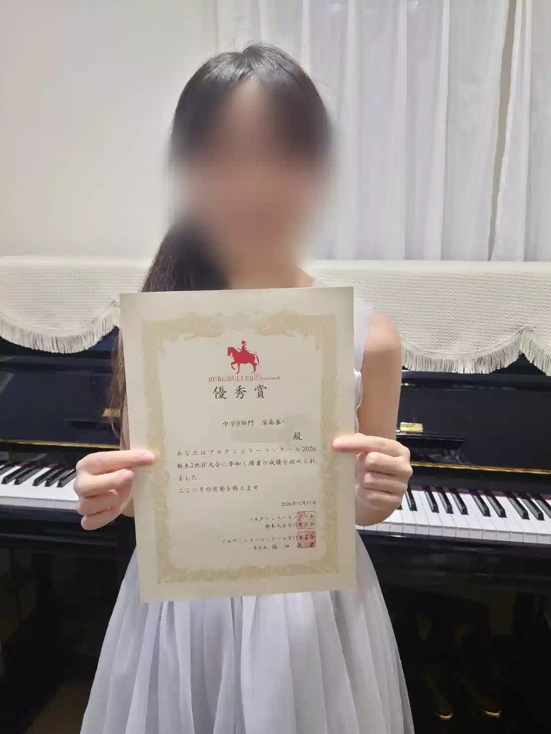 小山市のピアノ教室N piano music schoolの中学生の生徒がブルグミュラーコンクールで優秀賞を受賞、ピアノの前で賞状を持ち笑顔の写真